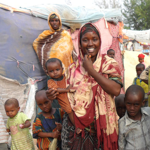 Une femme souriante se tient devant une tente avec sa famille.