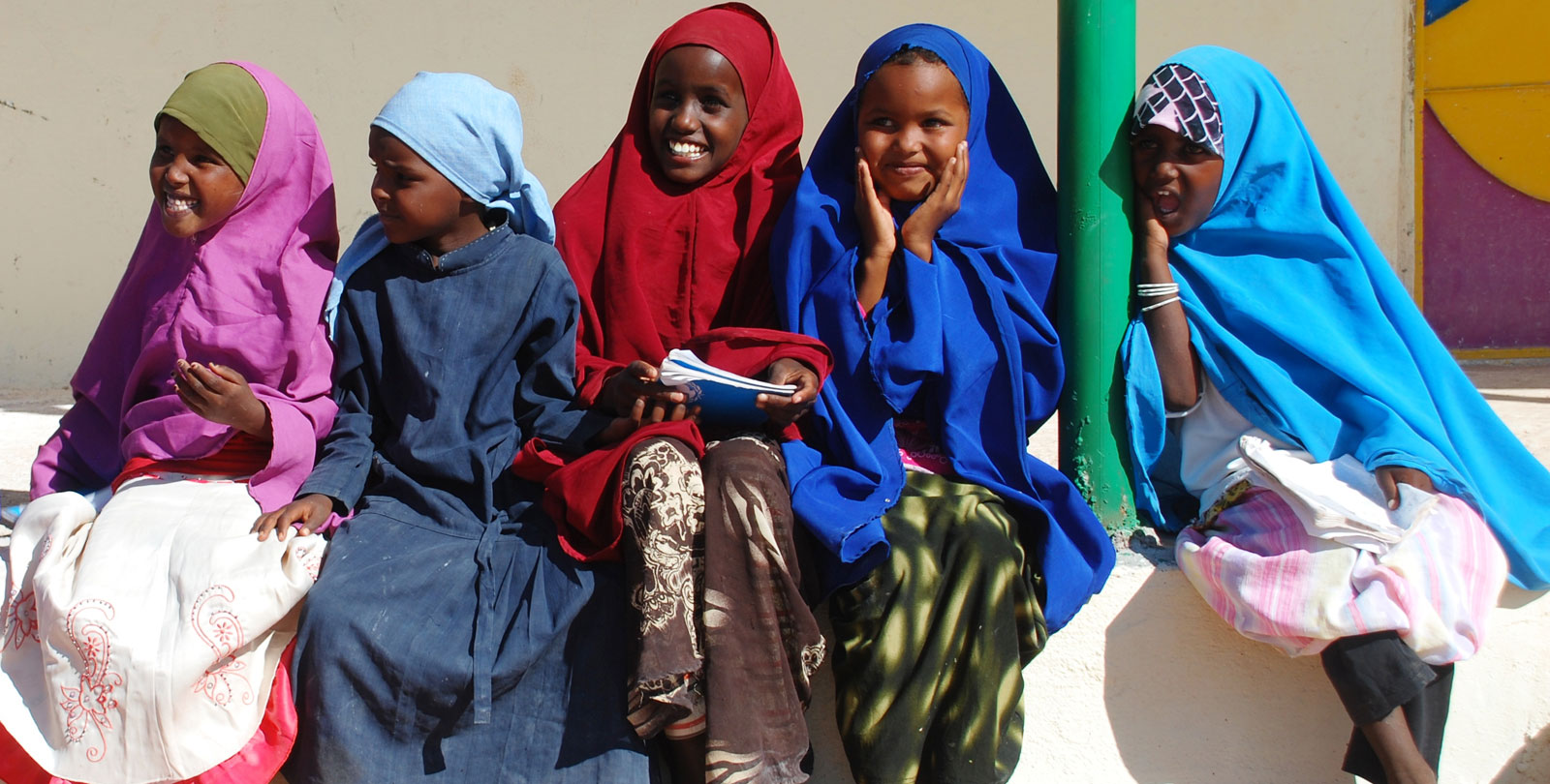 Cinq enfants somalien sont assis sur un mur et rigolent.