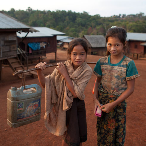 Deux filles regardent la caméra. Une fille porte un bidon d'eau sur son épaule. 