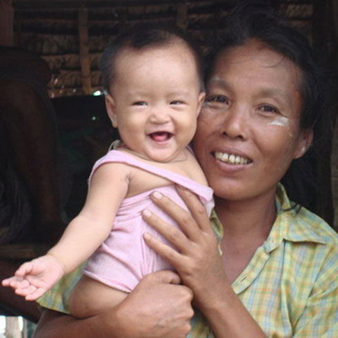 Une femme porte un bébé sur son bras et sourit.