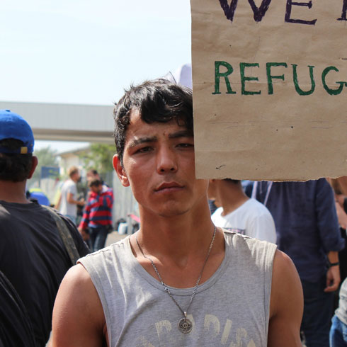 Un adolescent tient un panneau avec l'écriteau "We are refugees".