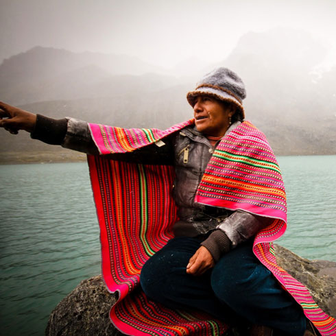 Une homme est asis au bord d'un lac et pointe le doigt à l'horizon.  