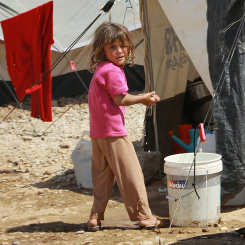 Une fille se tient devant une tente pour des réfugiés.