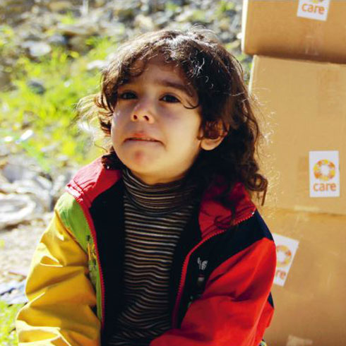 Un enfant est assis devant un tas de colis CARE.