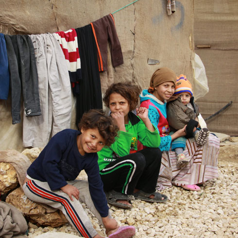 Une femme est assise avec ses enfants devant une maison en pierre.