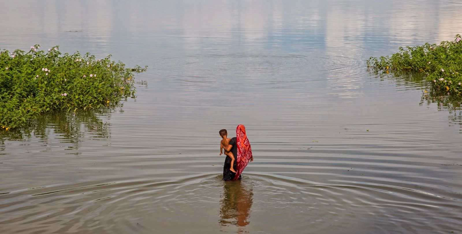 Une femme marche dans l'eau en portant un enfant dans ses bras.