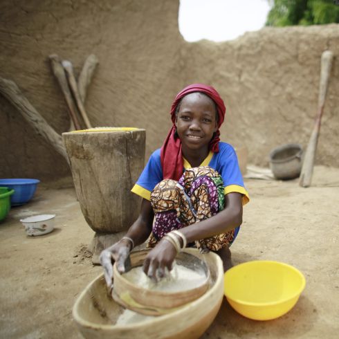 Une fille tamise de la farine de manioc